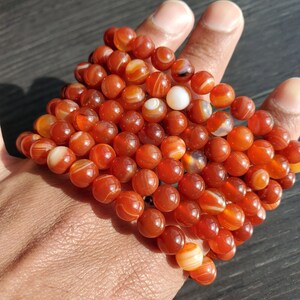 May include: A stack of carnelian gemstone bracelets with red and white stripes. The bracelets are made of round beads and are strung on elastic.