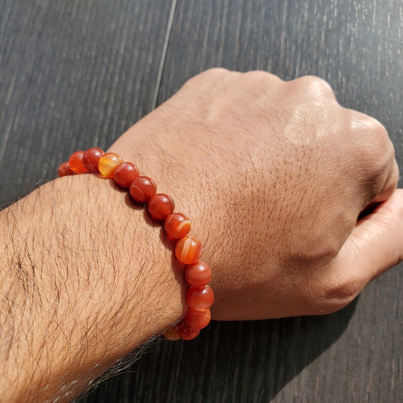 May include: A red carnelian gemstone bracelet with a stretchy band. The bracelet is made of round beads with a natural, polished finish.