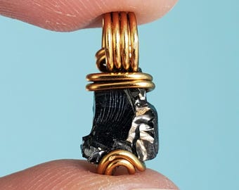 May include: A small, black, rough-textured stone pendant wrapped in gold wire. The stone has a metallic sheen and is set in a simple wire wrap.