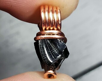 May include: A black obsidian crystal pendant wrapped in copper wire. The pendant is shaped like a rough, natural crystal with a copper loop at the top.