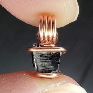 May include: A black gemstone pendant wrapped in copper wire. The wire is wrapped around the stone in a spiral pattern, creating a unique and stylish design.