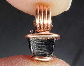 Könnte beinhalten: Ein schwarzer Edelstein-Anhänger, der mit Kupferdraht umwickelt ist. Der Draht ist spiralförmig um den Stein gewickelt und erzeugt ein einzigartiges und stilvolles Design.