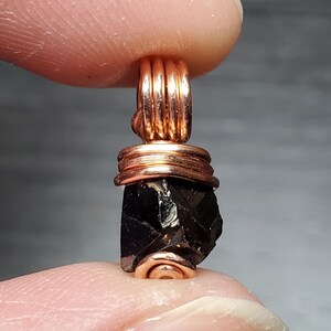 May include: A black gemstone pendant wrapped in copper wire. The pendant is faceted and has a rough, natural look.