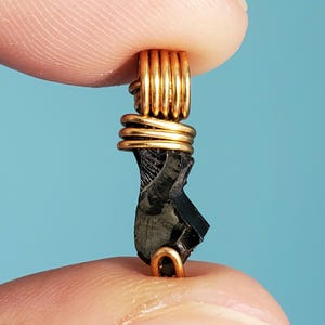 May include: A black stone pendant wrapped in gold wire. The stone is irregularly shaped and has a rough texture. The wire is wrapped around the stone in a spiral pattern.