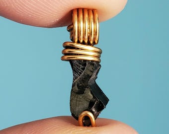 May include: A black stone pendant wrapped in gold wire. The stone is irregularly shaped and has a rough texture. The wire is wrapped around the stone in a spiral pattern.
