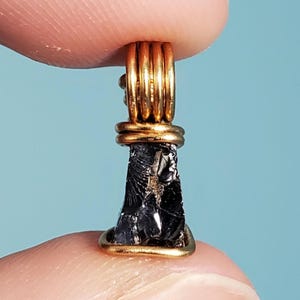 May include: A black obsidian stone pendant wrapped in gold wire. The stone is rough and has a natural, irregular shape.