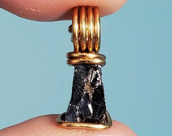 May include: A black obsidian stone pendant wrapped in gold wire. The stone is rough and has a natural, irregular shape.