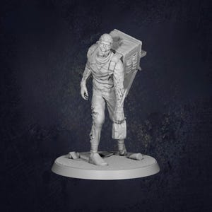 May include: A grayscale figurine of a zombie-like figure carrying a large box on its back. The figure is wearing tattered clothing and has exposed flesh. The figurine is standing on a circular base with debris scattered around.