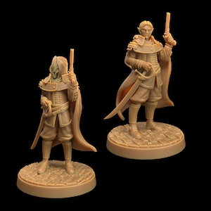 Può includere: Due figure in miniatura di persone vestite con abiti marroni e dorati e che tengono pistole. Le figure sono in piedi su basi rotonde con una texture simile alla pietra.