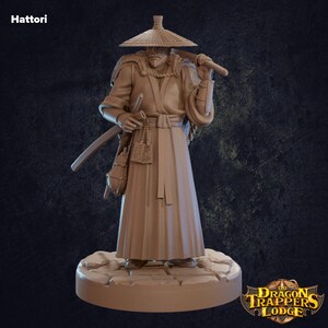 May include: A brown painted miniature figurine of a man wearing a wide-brimmed straw hat, a long robe, and carrying a sword. The figurine is standing on a circular base with a stone-like texture. The text "The Dragon Trappers Lodge" is visible in the lower right corner of the image.