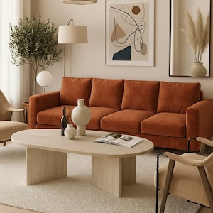 May include: A living room scene featuring a rust-colored sofa, a light wood oval coffee table, and two beige armchairs. Decorative vases and a bottle sit on the table. A framed abstract art piece hangs on the wall.