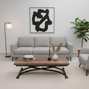 Peut inclure: Un salon moderne avec un canapé gris, une table basse en bois avec une base en métal noir et une œuvre d'art abstraite encadrée. Un lampadaire et une plante en pot complètent le décor. La pièce est meublée d'un fauteuil gris et d'un tapis clair.