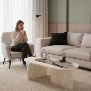 Peut inclure: Un salon moderne aux tons neutres. Il comprend un canapé clair, un fauteuil et une table basse en marbre. Une femme est assise dans le fauteuil, tenant une tasse. La pièce est décorée d'un décor minimaliste, dont une suspension.