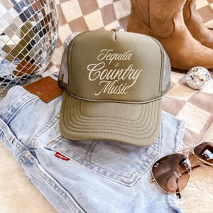 Olive green foam front trucker hat with cream “Tequila & Country Music” lettering, styled with denim jeans and disco ball accents.