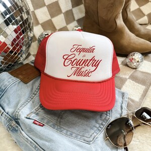 Red and white foam front trucker hat with red “Tequila & Country Music” lettering, styled on denim jeans with western accessories.