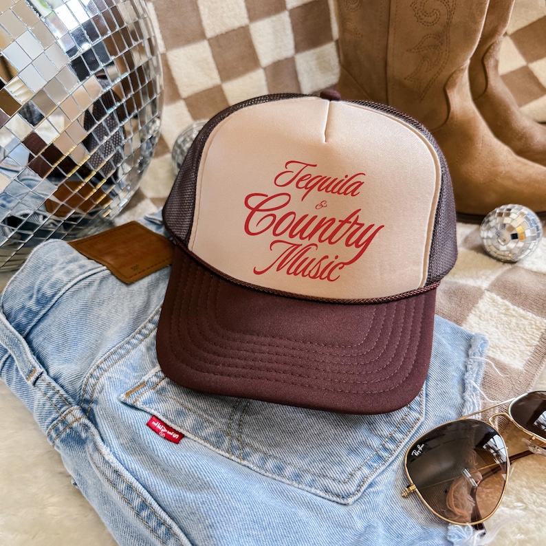 Brown and tan foam front trucker hat with “Tequila & Country Music” text, styled on denim jeans with disco ball and cowboy boots.
