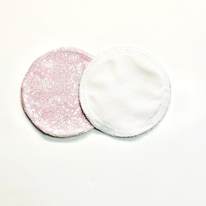 May include: Two circular reusable nursing pads. One has a pink floral design, the other is white. The pads are made from soft, absorbent fabric, designed for comfort and leak protection. Suitable for environmentally conscious mothers.