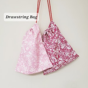 Peut inclure: Deux sacs à cordon avec des motifs floraux. Le sac de gauche est rose avec des fleurs blanches, et le sac de droite est rouge avec des fleurs blanches. Les deux sacs ont des cordons de serrage rouges.