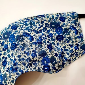 K&ouml;nnte beinhalten: Eine blaue und wei&szlig;e Gesichtsmaske mit floralem Muster und schwarzen elastischen Ohrschlaufen.