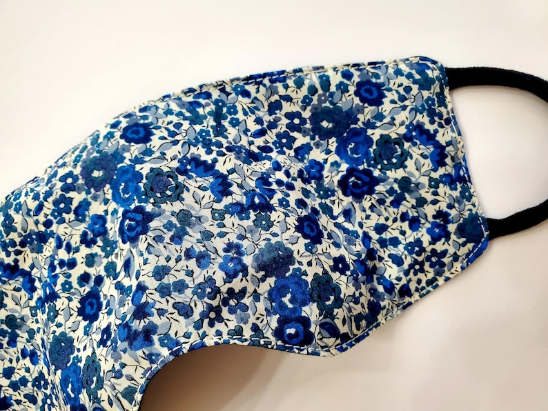 K&ouml;nnte beinhalten: Eine blaue und wei&szlig;e Gesichtsmaske mit floralem Muster und schwarzen elastischen Ohrschlaufen.