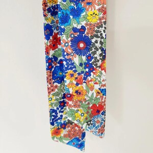 Puede incluir: Bufanda con estampado floral que presenta una vibrante variedad de flores en rojo, azul, amarillo y naranja sobre un fondo blanco. La bufanda est&aacute; hecha de una tela ligera y es ideal para a&ntilde;adir un toque de color a cualquier atuendo.