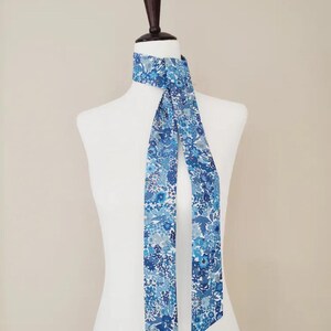 Puede incluir: Una bufanda azul con estampado floral est&aacute; drapeada sobre un maniqu&iacute; blanco. La bufanda presenta una variedad de tonos azules, claros y oscuros, con un delicado dise&ntilde;o floral. La bufanda es de tela suave y es un accesorio elegante.