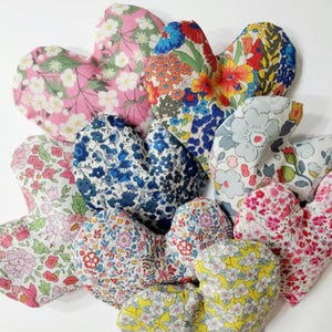 Puede incluir: Una colecci&oacute;n de art&iacute;culos de tela en forma de coraz&oacute;n con varios estampados florales. Los corazones presentan una gama de colores, incluyendo rosa, azul, rojo y amarillo, con dise&ntilde;os florales detallados. Los art&iacute;culos son probablemente decorativos o funcionales, como saquitos o almohadas.