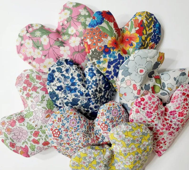 Puede incluir: Una colecci&oacute;n de art&iacute;culos de tela en forma de coraz&oacute;n con varios estampados florales. Los corazones presentan una gama de colores, incluyendo rosa, azul, rojo y amarillo, con dise&ntilde;os florales detallados. Los art&iacute;culos son probablemente decorativos o funcionales, como saquitos o almohadas.