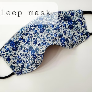 K&ouml;nnte beinhalten: Eine blaue und wei&szlig;e Blumen-Schlafmaske mit einem schwarzen Gummiband.