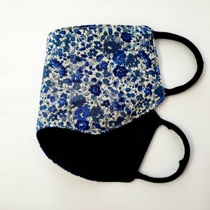 K&ouml;nnte beinhalten: Eine blaue und wei&szlig;e, mit Blumen gemusterte Stoffmaske mit schwarzem Stofffutter und verstellbaren Ohrschlaufen.