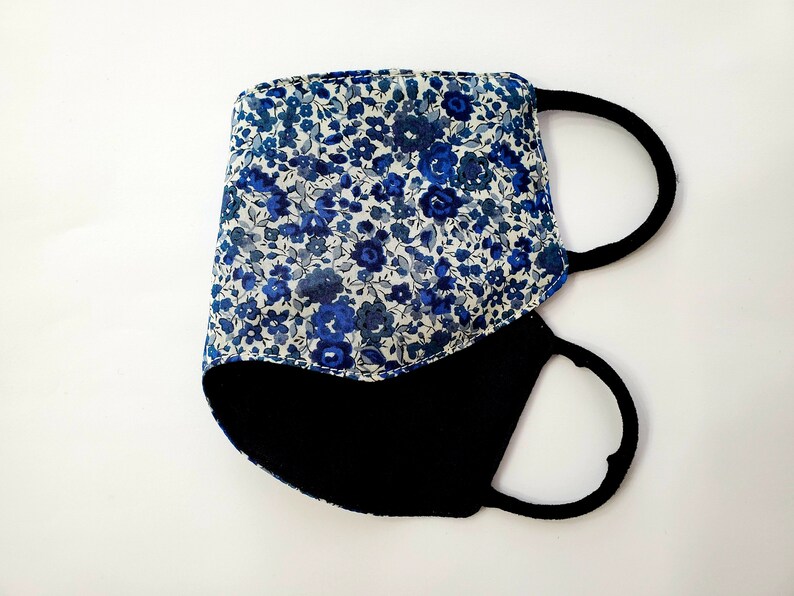 K&ouml;nnte beinhalten: Eine blaue und wei&szlig;e, mit Blumen gemusterte Stoffmaske mit schwarzem Stofffutter und verstellbaren Ohrschlaufen.