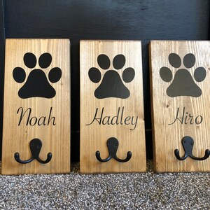 May include: Three wooden dog leash hooks with black paw prints and the names Noah, Hadley, and Hiro.