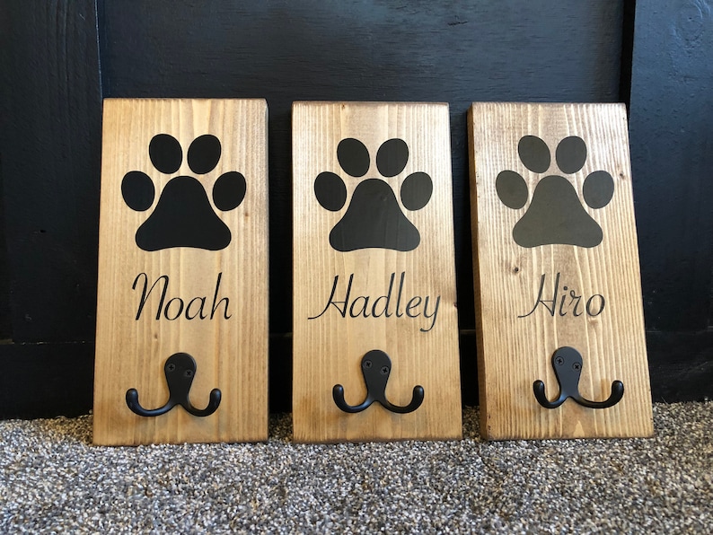 May include: Three wooden dog leash hooks with black paw prints and the names Noah, Hadley, and Hiro.