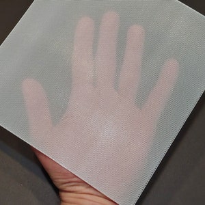 Peut inclure: Tissu en maille de nylon blanc à tissage fin. Le tissu est translucide et présente une surface légèrement texturée.