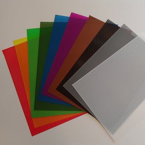 May include: A collection of ten different coloured sheets of plastic, arranged in a fan shape. The colours are yellow, orange, green, blue, purple, brown, black, grey, and white.