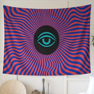 May include: A wall tapestry with a vibrant, psychedelic design. The tapestry features a central black circle with a teal eye symbol, surrounded by red and blue wavy stripes radiating outwards. The overall aesthetic is reminiscent of retro art.