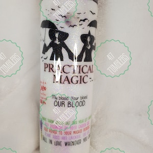 May include: A white glitter tumbler with a black lid. The tumbler features the words "PRACTICAL MAGIC" and illustrations of witches. Additional text includes "My blood. Your blood. OUR BLOOD." and a list of instructions.