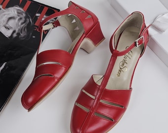 May include: A pair of red T-strap shoes with a low block heel, featuring cut-out details on the sides and a silver-toned buckle closure. The interior insole is light-coloured and displays the text "Harlow Shoes" in a cursive black font.