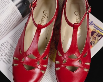 May include: A pair of red leather t-strap shoes with cut-out detailing. The shoes have a gold label that reads "Harlem" on the inside.