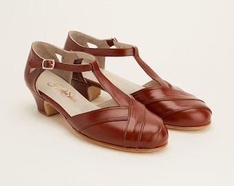 May include: A pair of brown leather heeled shoes with a T-strap design. The shoes have a buckle closure and are made by "Fletcher Shoes".
