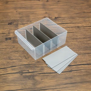 May include: A clear plastic storage box with four gray dividers. The box is empty, but there are three extra gray dividers next to it.