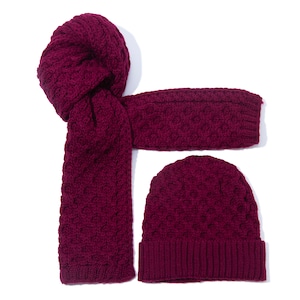 May include: A burgundy knitted hat and matching scarf set. The hat is a beanie style with a folded brim. The scarf is a long, rectangular shape with a cable knit pattern.