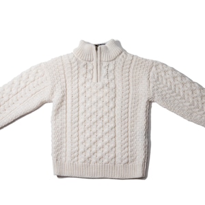 May include: A white cable knit sweater with a mock neck and a zipper.