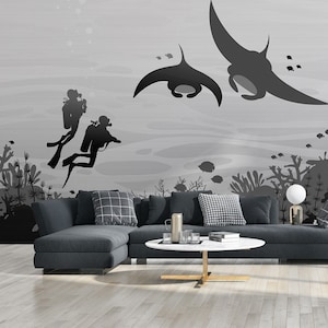 May include: A modern living room with a gray sectional sofa, a white coffee table, and a large wall mural featuring manta rays and scuba divers. A tall bamboo plant in a white pot adds a natural element. The room has hardwood floors and large windows.
