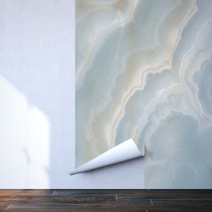 May include: A close-up of a white wall with a section of blue and white marble wallpaper peeling back to reveal the white wall underneath.