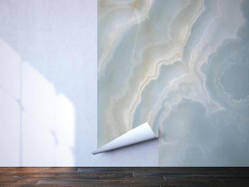 May include: A close-up of a white wall with a section of blue and white marble wallpaper peeling back to reveal the white wall underneath.