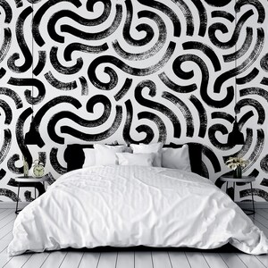 May include: A white bedroom with a bed featuring white bedding and black throw pillows. The wall behind the bed is covered in a black and white abstract pattern wallpaper.