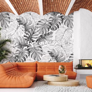 May include: A living room interior with an orange sectional sofa, a coffee table, and a fireplace. The wall behind the sofa is decorated with a black and white tropical leaf wallpaper.