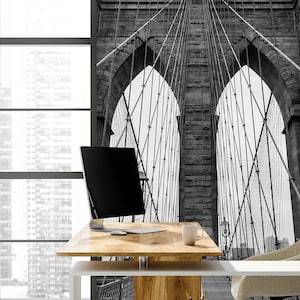 May include: A black and white photo of the Brooklyn Bridge in New York City. The photo is used as a wall mural in a modern office space with a white desk, a computer, and a chair.