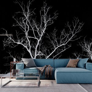 May include: A teal sectional sofa with a throw blanket and pillows in front of a black and white wall mural of bare branches.